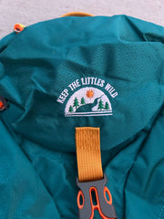 Teal bag with 'Keep the Littles Wild' logo and orange strap on a gray surface