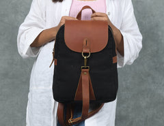 Person holding a black backpack with brown leather straps against a gray background