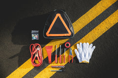 Roadside emergency kit with triangle warning sign, gloves, and tools on a black surface with yellow stripes.