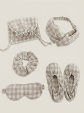 Set of gray plaid sleep accessories including a bonnet, headband, eye mask, slippers, and a drawstring bag on a beige background.