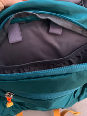 Close-up of a teal backpack with a zipper open, showing black interior.