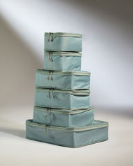 Set of four light blue packing cubes stacked on a neutral background