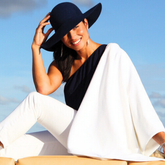 Woman wearing a black hat and white outfit against a blue sky.