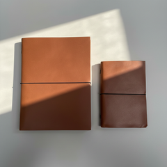 Two brown leather notebooks on a light gray surface with soft shadows.