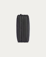 A black zippered pouch with a vertically pleated or ribbed texture, shown from the back against a solid off-white background.