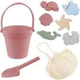 Set of beach toys including a pink bucket, shovel, and net with animal-shaped molds on a white background.