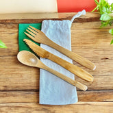 Set of bamboo cutlery including a spoon, knife, and two forks on a wooden surface with a cloth underneath.