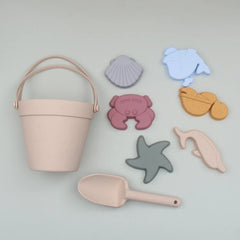 Set of children's sand toys including a pink bucket, shovel, and sea creature molds on a light gray background.