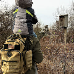 Person with a child on their shoulders wearing a large backpack in a natural setting.