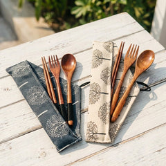 Wooden cutlery set with black handles on patterned cloths on a wooden surface.