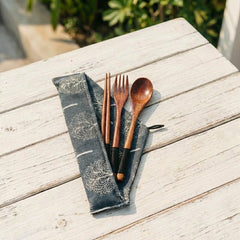 Wooden cutlery set on a folded dark gray napkin with floral patterns on a wooden surface.