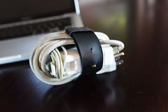 Coiled white cable with a black leather strap on a dark surface, blurred laptop in the background