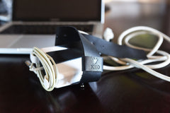 Black belt with a visible brand logo on a wooden surface next to a laptop.