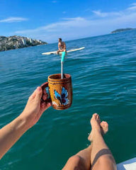Person holding a cup with a butterfly design on a body of water with another person in the background.