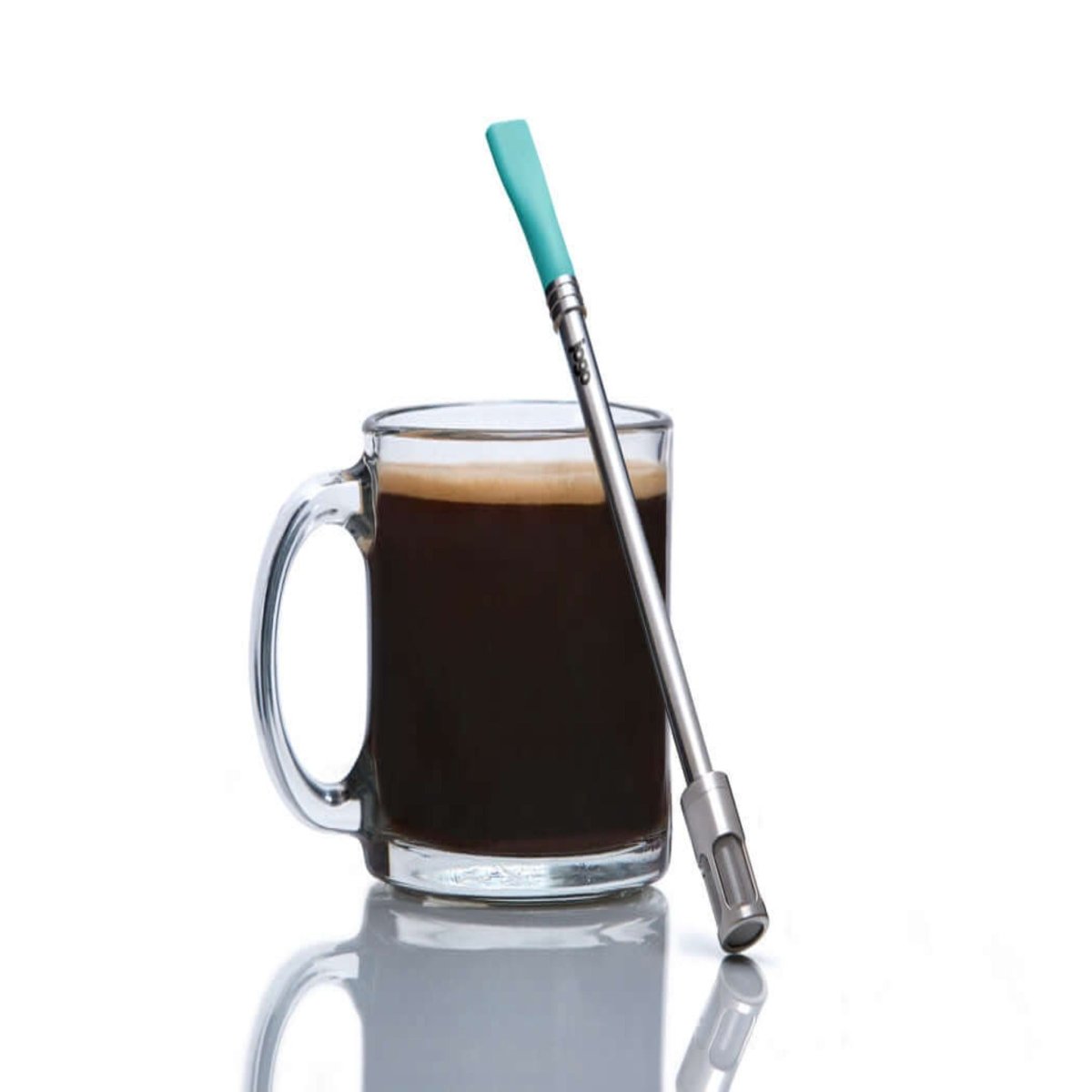 Clear glass mug with coffee and a metal straw with turquoise top on a white background