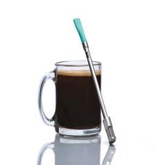 Clear glass mug with coffee and a metal straw with turquoise top on a white background