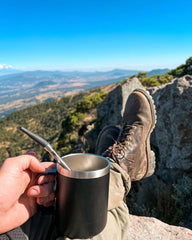 Person holding a thermos with a scenic mountain view in the background