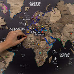World map with countries labeled, hand placing a red marker on a specific location.