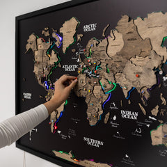 World map with wooden relief and pins, hand placing a pin on the map.