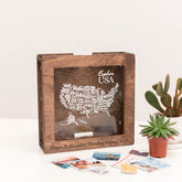 Wooden box with USA map design on a white surface with plants.