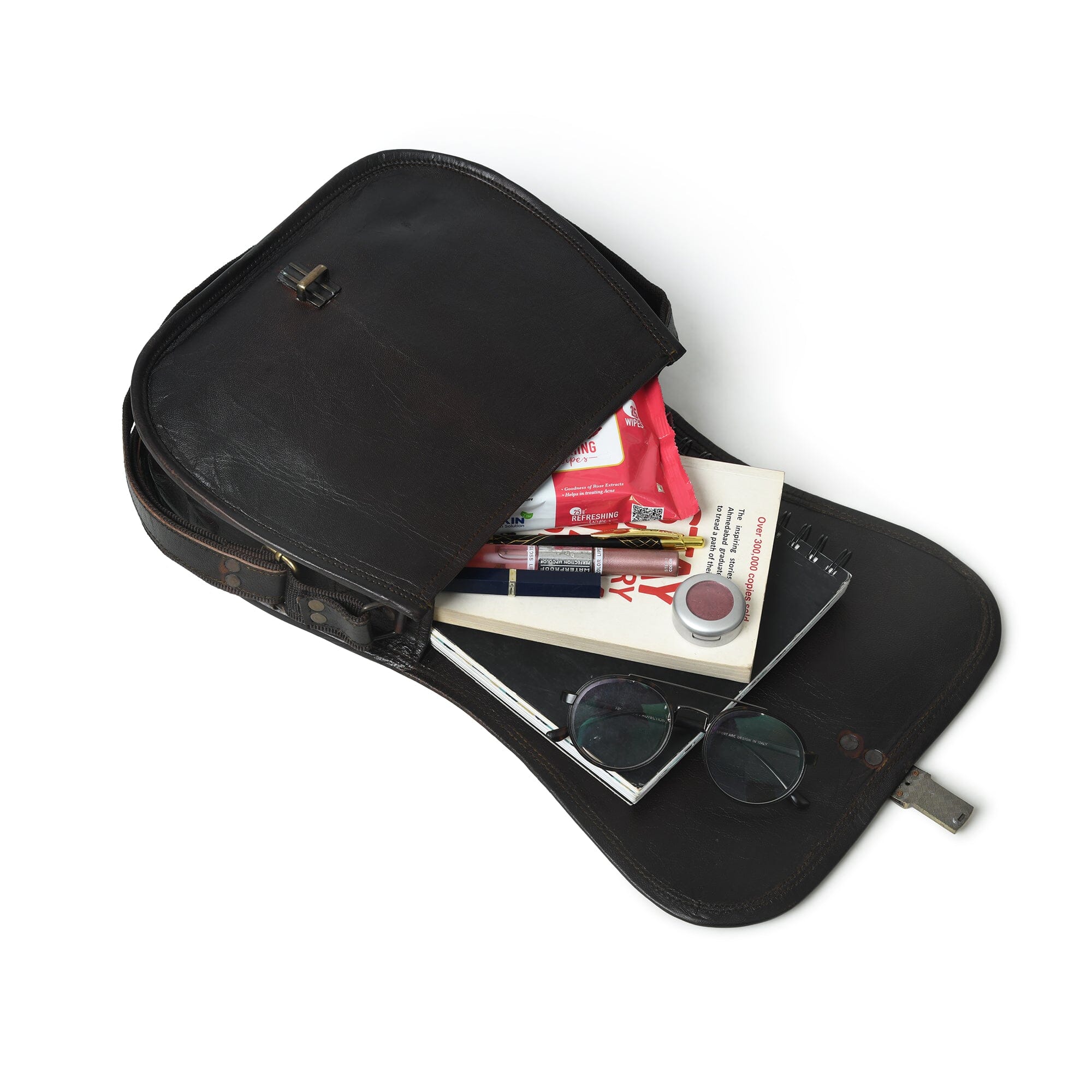 Black leather briefcase with items including a book, sunglasses, and a pen on a white background