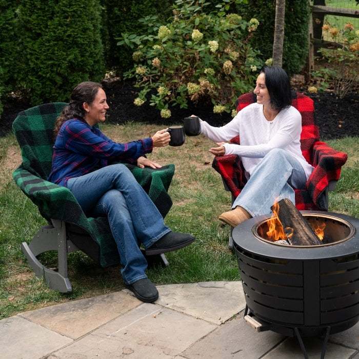 Two people sitting in chairs by a fire pit in a garden setting.