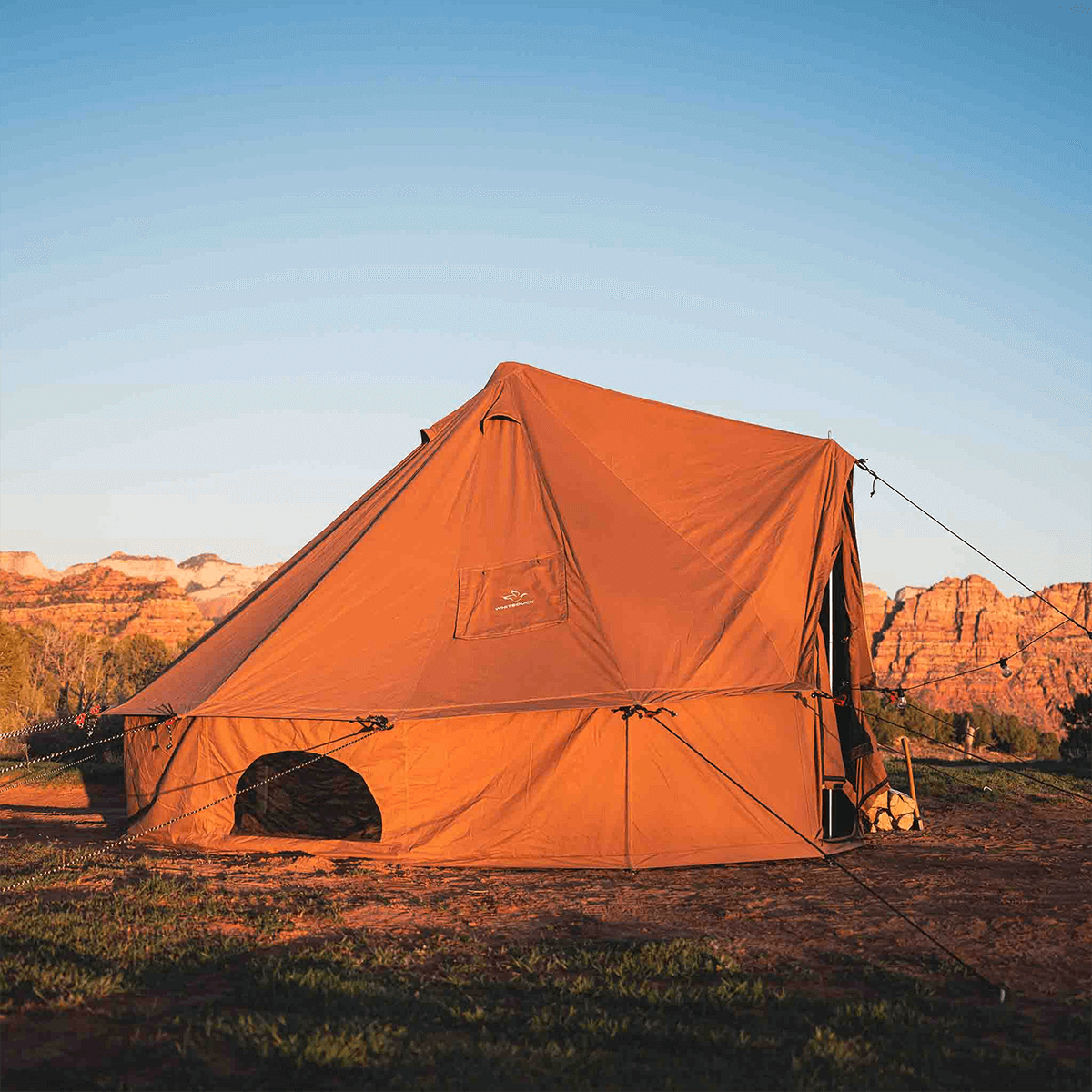 Orange tent set up in a desert landscape with mountains in the background