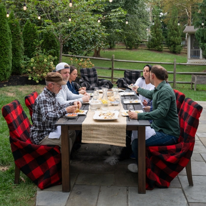 Group of people dining outdoors at a table with red and black checkered chairs.