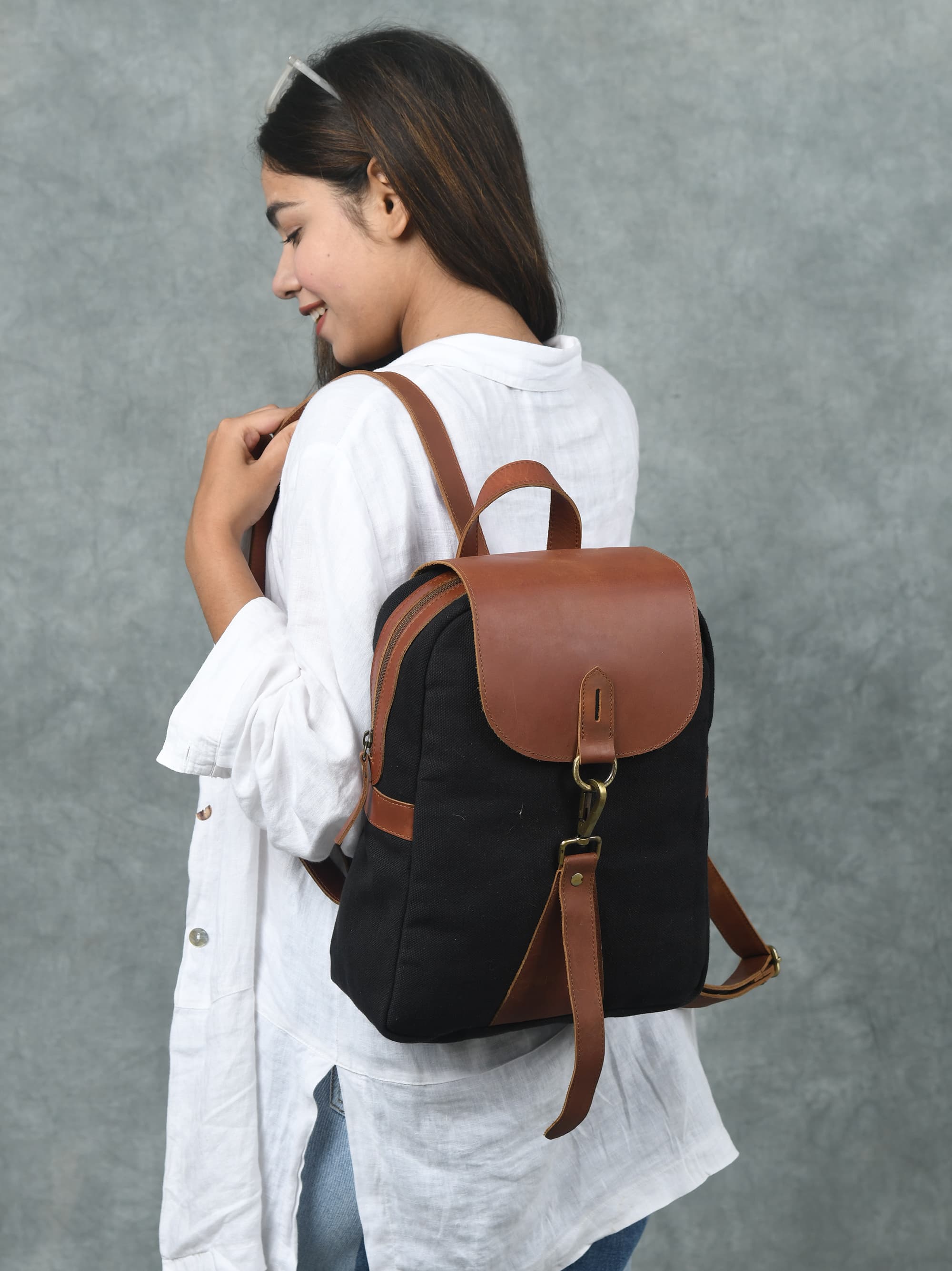 Woman wearing a black backpack with brown leather straps against a gray background