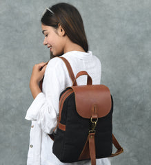 Woman wearing a black backpack with brown leather straps against a gray background