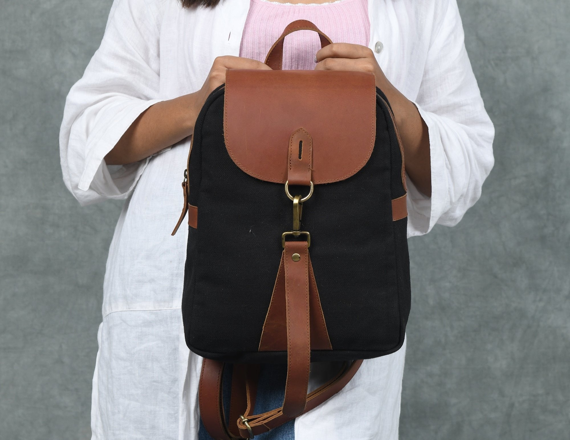 Person holding a black backpack with brown leather straps against a gray background