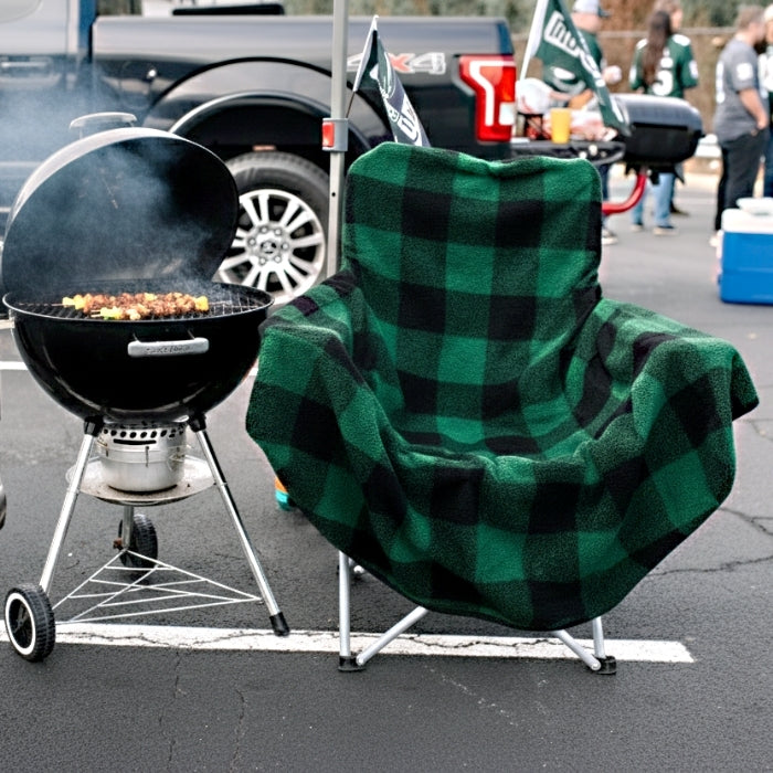 Green and black checkered chair next to a grill with food in a tailgating setting.
