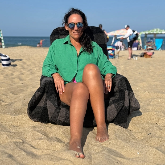 Woman sitting on a beach chair at the beach wearing sunglasses and a green shirt.