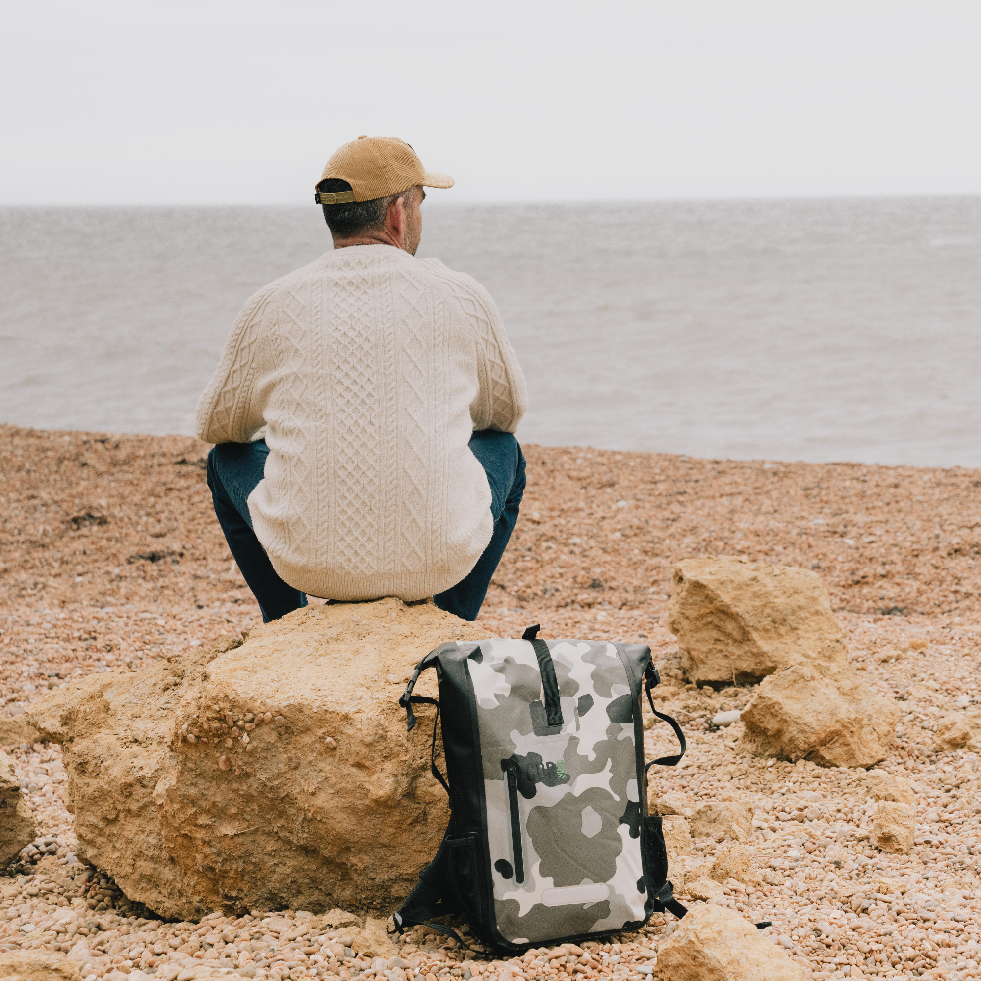 Man sitting on a rock by the sea with a camouflage backpack
