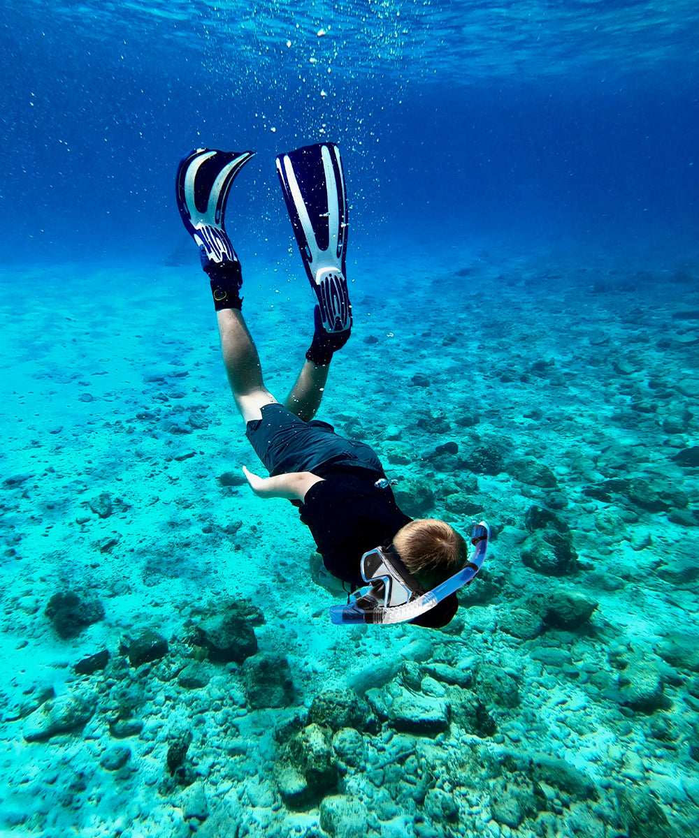 Person snorkeling underwater in clear blue water with coral reef