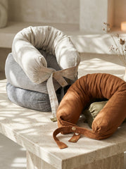 Three travel neck pillows in white, gray, and brown on a stone surface with a neutral background.