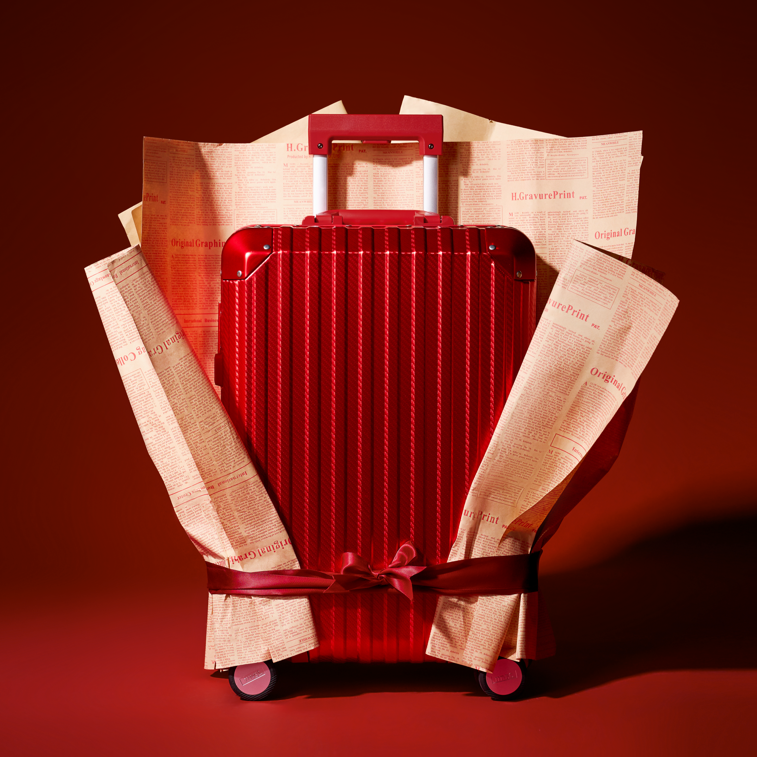 Red suitcase wrapped with a ribbon on a red background