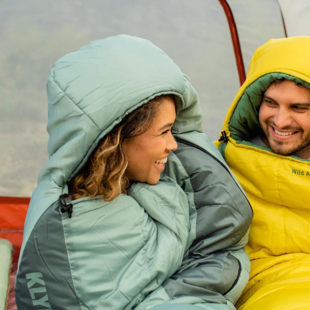 Two people wearing insulated sleeping bags sitting close to each other.