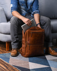 Person sitting on a couch with a brown leather backpack and a laptop.