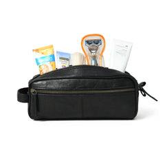 Black leather toiletry bag with various travel items on a white background