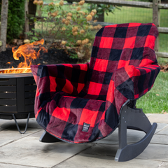 A red and black buffalo plaid fleece chair cover draped over a dark gray rocking chair on an outdoor patio, with a fire pit and garden in the background.