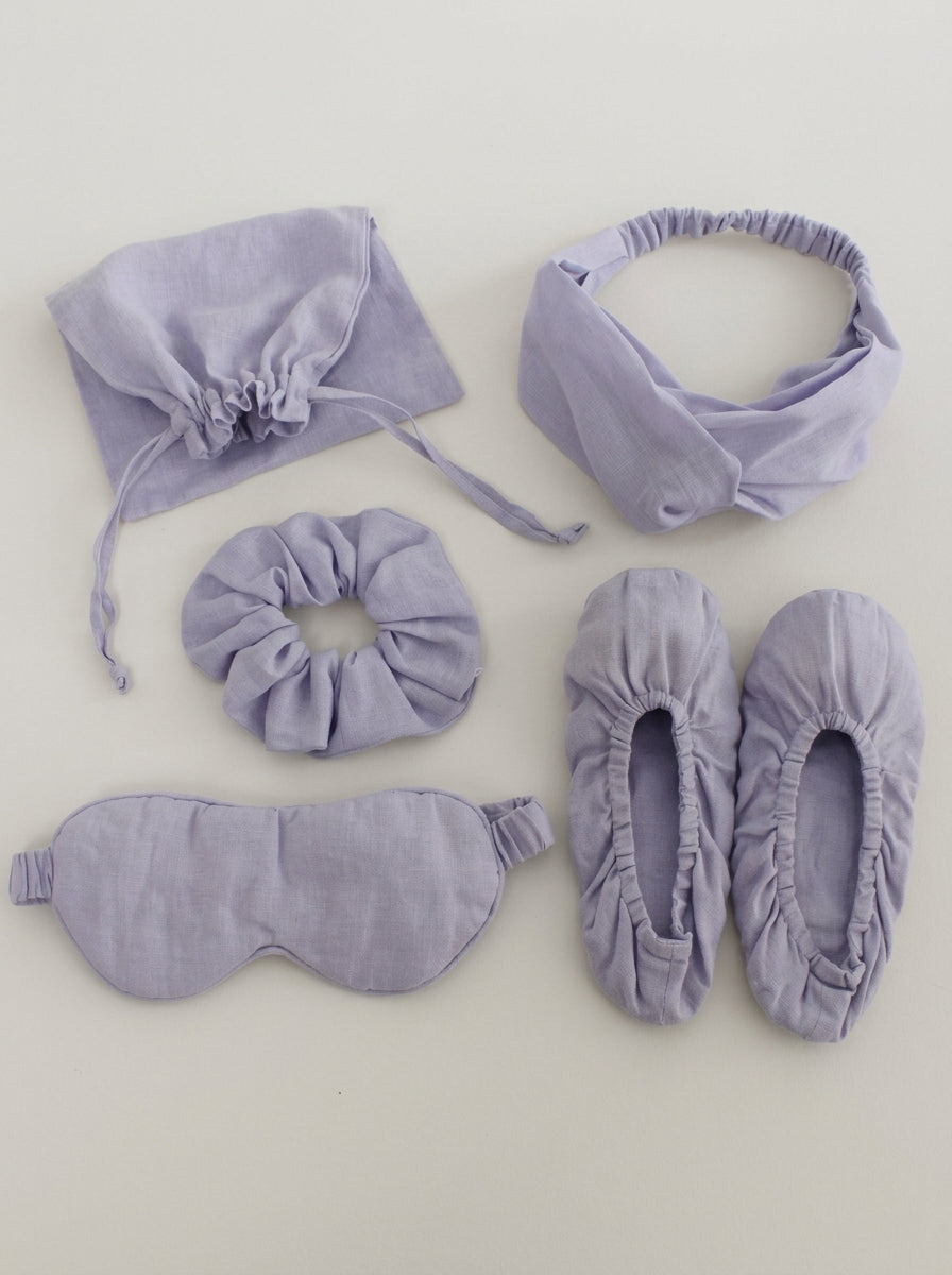 Set of lavender sleep accessories including a headband, eye mask, and slippers on a light gray background.