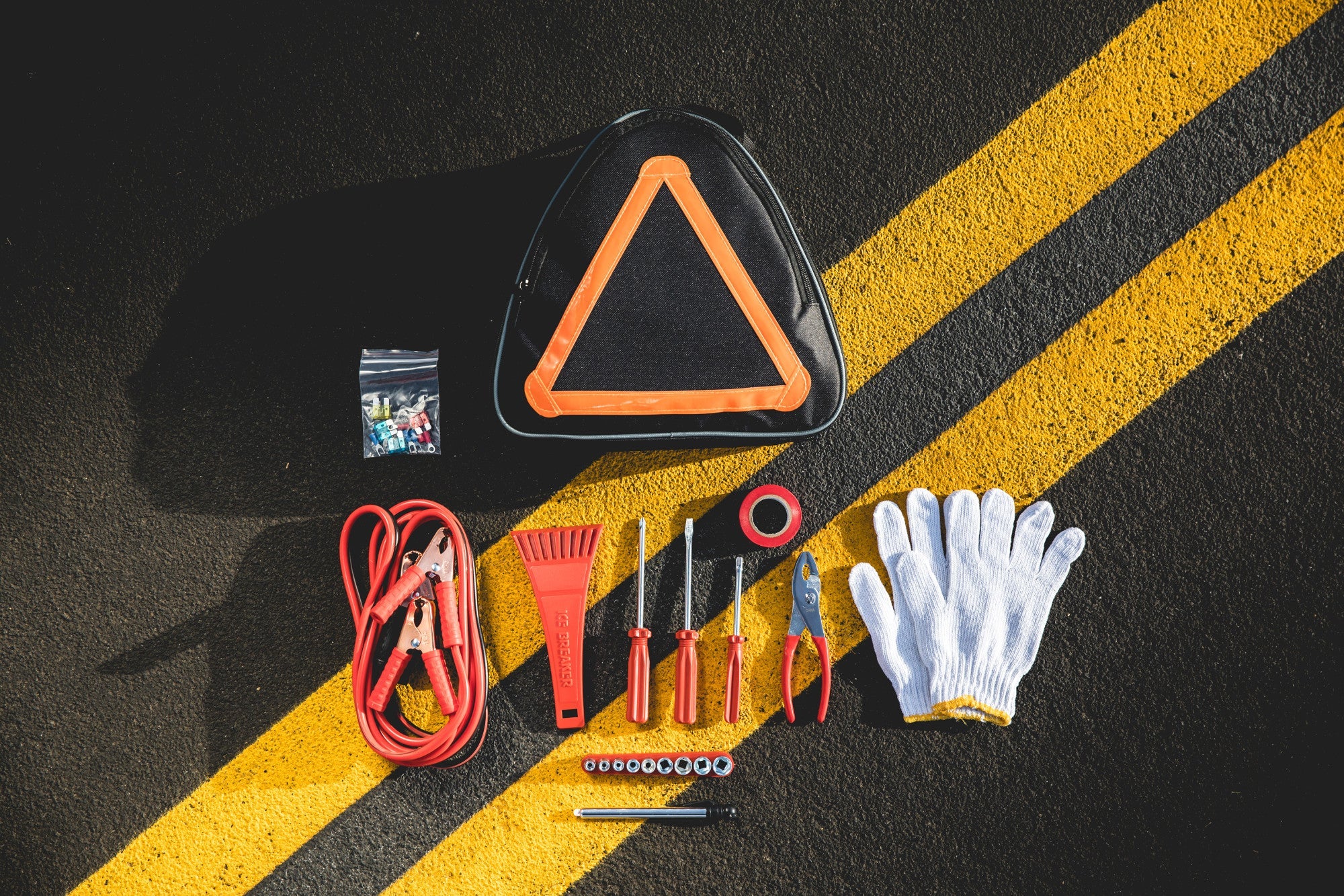 Roadside emergency kit with triangle warning sign, gloves, and tools on a black surface with yellow stripes.