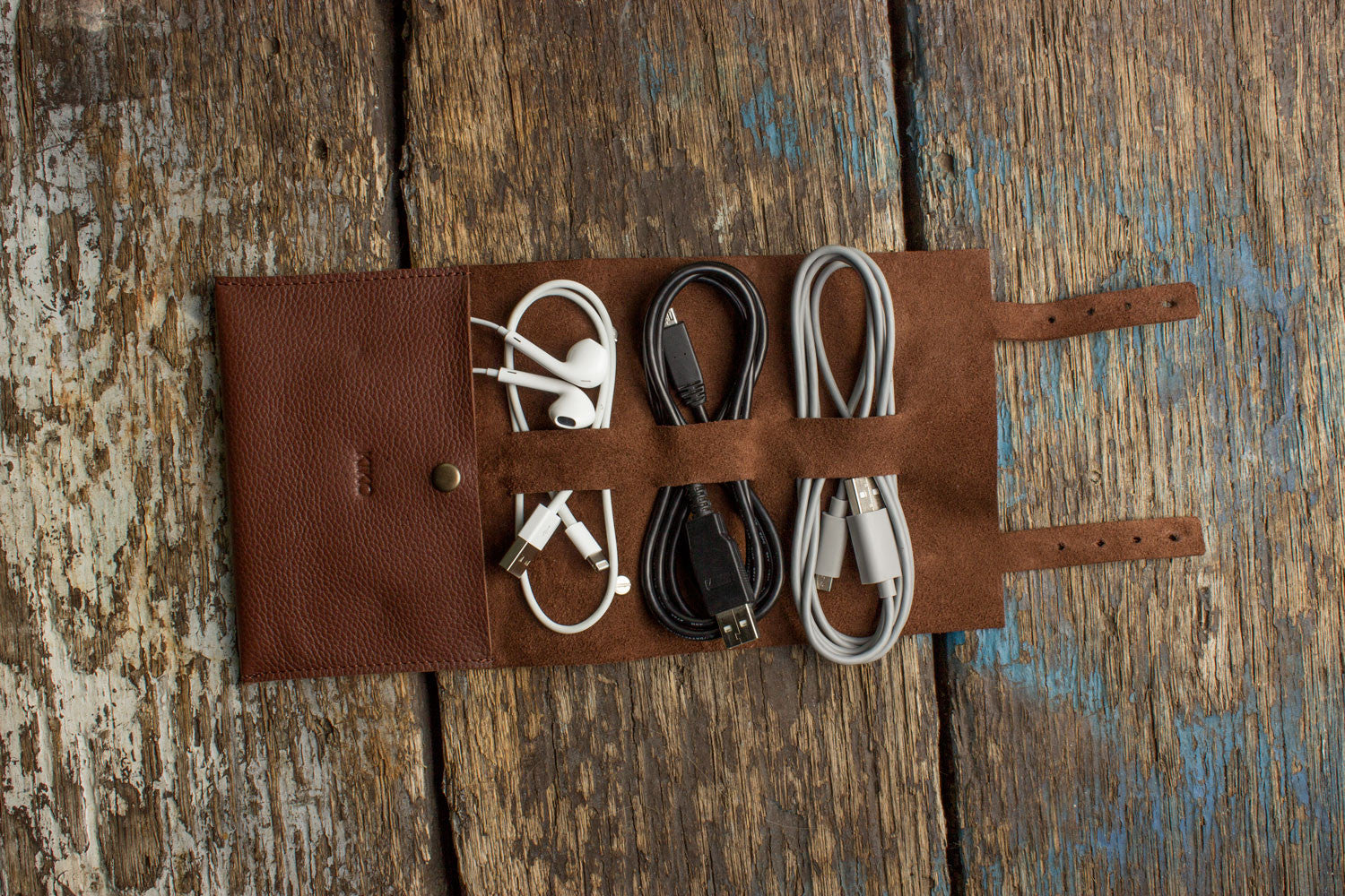 Brown leather roll-up organizer with electronic cables on a wooden surface