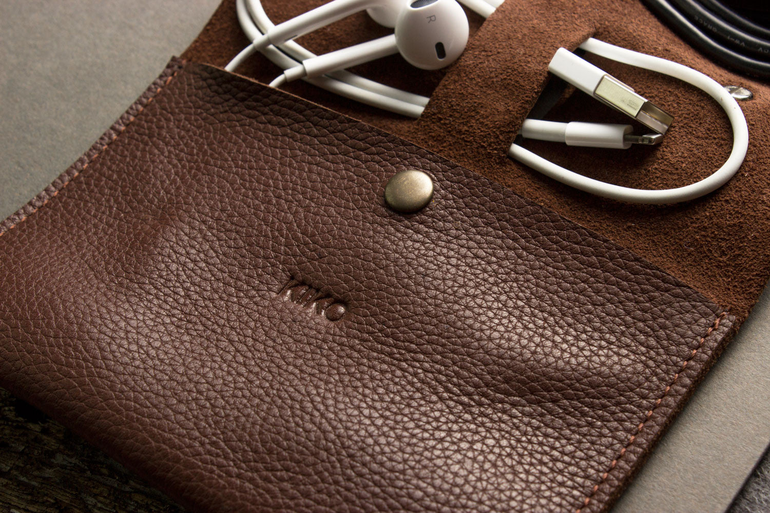 Brown leather pouch with earbuds and a USB cable on a gray surface