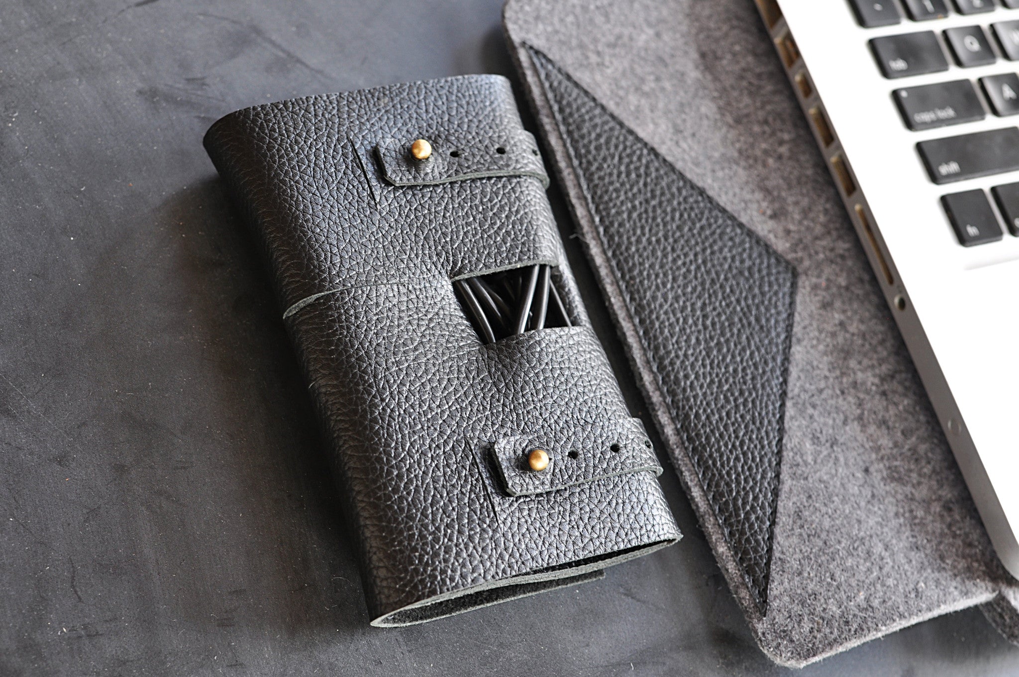 Black leather wallet with gold accents on a gray surface next to a laptop.