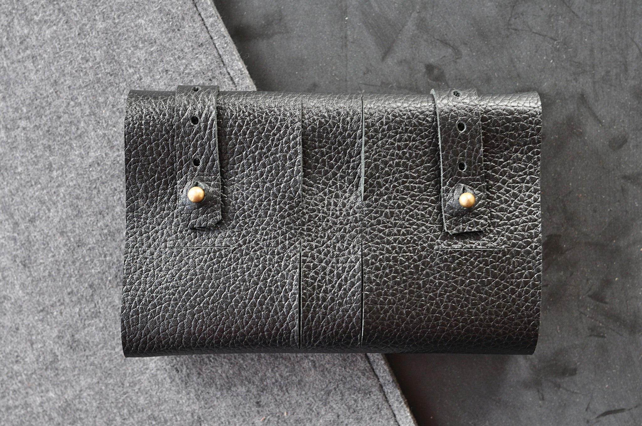 Black leather wallet with gold studs on a textured gray surface