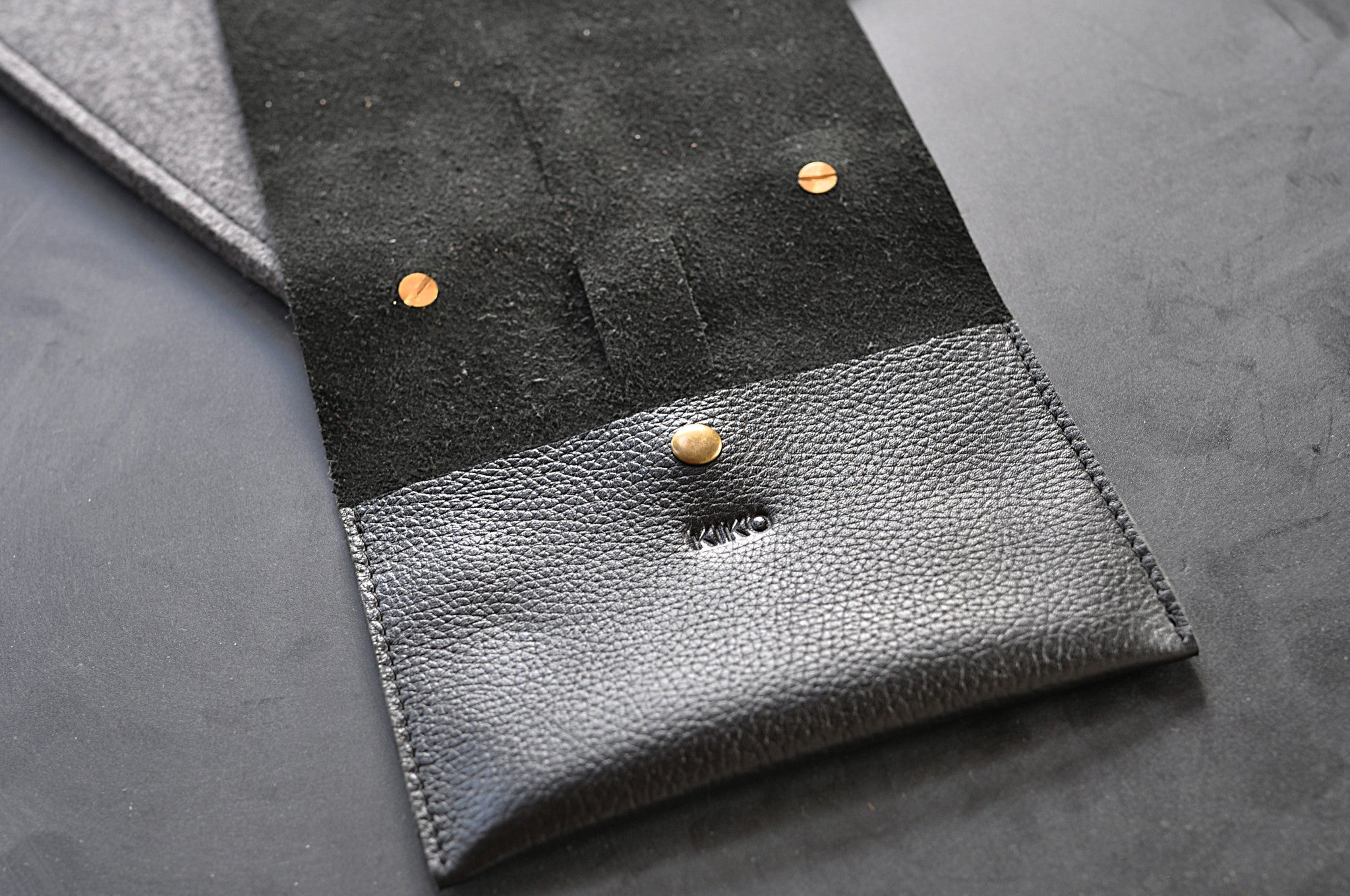 Close-up of a black and gray leather wallet with gold buttons on a dark surface