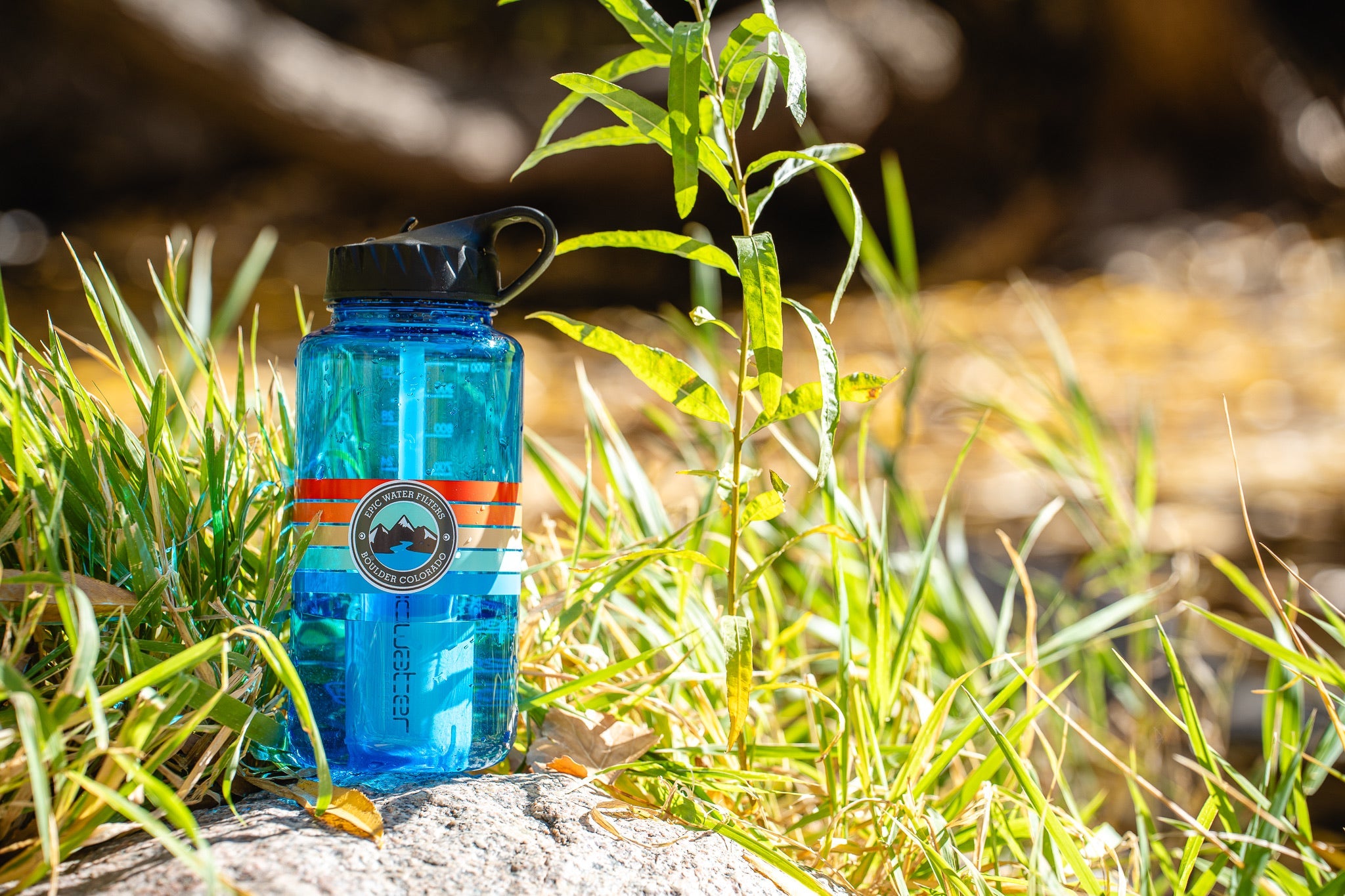 Blue water bottle with a logo on a rock surrounded by grass