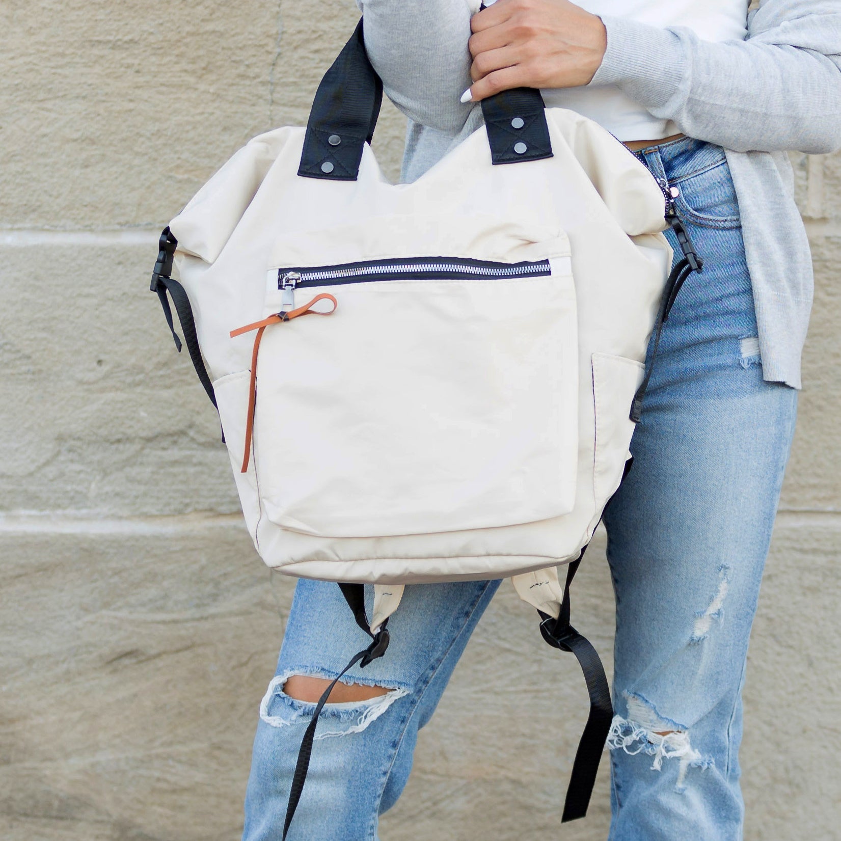 Person holding a beige backpack with a stone wall background